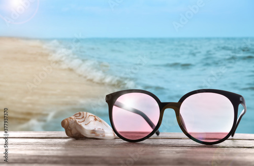 Shell and stylish sunglasses on wooden table near sea with sandy beach
