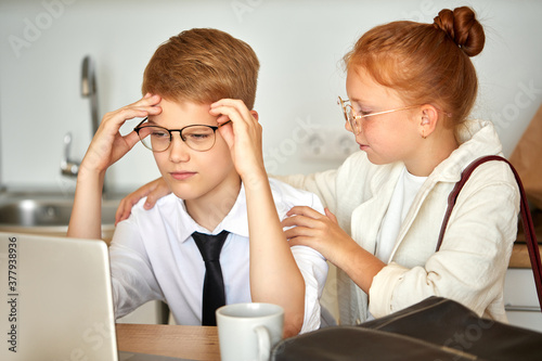 adorable redhead child girl supports boyfriend boy working on laptop, she is listening to his problems at work, deadlines. at home