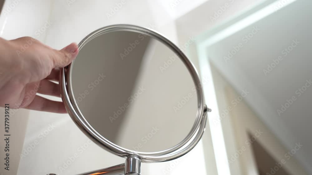Closeup view 4k video of elegant round magnifying mirror attached to wall in bathroom interior.