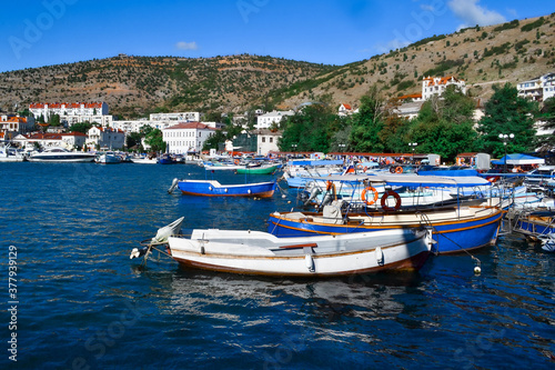 white colorful ships and boats in water at piers among houses of town balaclava near rocks of mountains, reflections in ripples