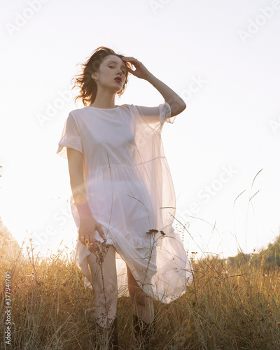 
A girl in a white dress walks across the field at sunset