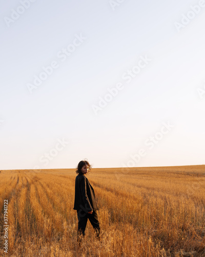 
A girl in a black suit walks across the field at sunset