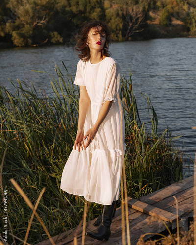 
A girl in a solid dress and black boots stands by the river