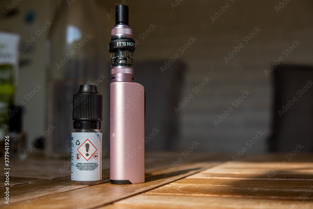 next to a bottle filled with liquids is a e-cigarette next to a bottle filled with liquids is a e-cigarette