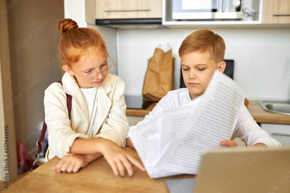 friendly kids couple behave themselves as adults, solve work problems together, look at laptop and documents, checking bills, making purchase online, freelance. children, people concept friendly kids couple behave themselves as adults, solve work problems together, look at laptop and documents, checking bills, making purchase online, freelance. children, people concept