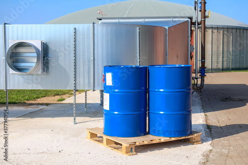 2 big blue barrels stand on a wooden pallet in front of a biogas plant