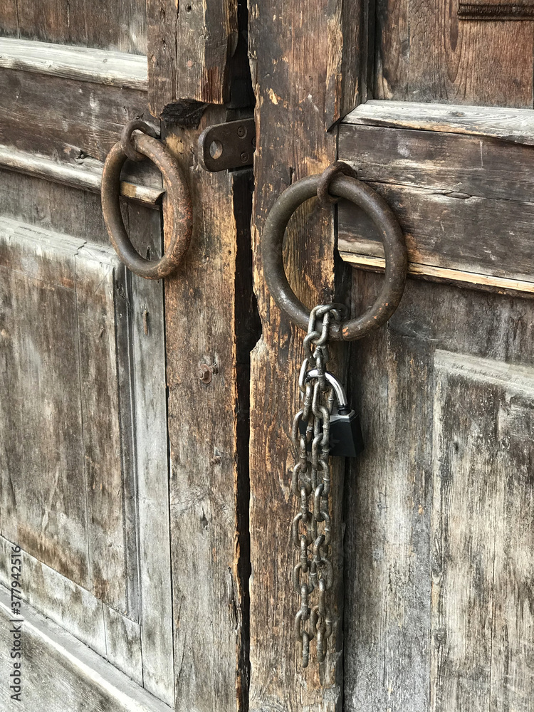 Ancient wooden gates with the round metal doorknobs and a hanging chain with a lock. Vertical orientation. Ancient wooden gates with the round metal doorknobs and a hanging chain with a lock. Vertical orientation.