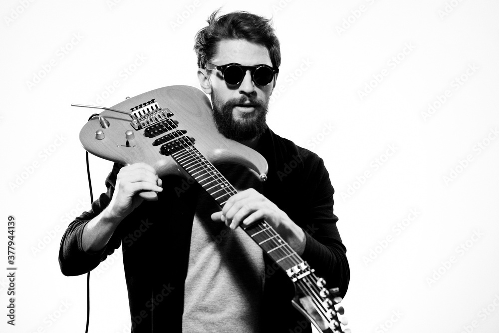 Obraz premium A man holds a guitar in his hands black leather jacket dark glasses music performance light background