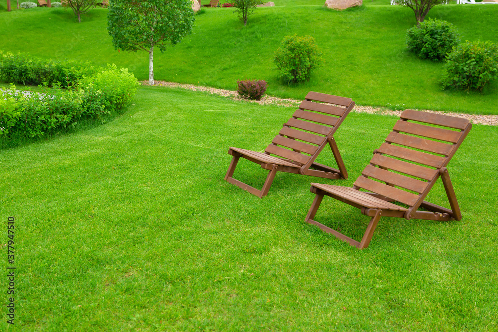 Recreation and tourism advertising. Two Empty brown wooden deck chair or chaise longue, on the green grass of a fresh lawn. Place for text Recreation and tourism advertising. Two Empty brown wooden deck chair or chaise longue, on the green grass of a fresh lawn. Place for text