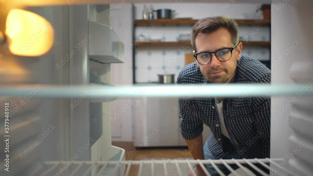 Hungry young man looking for food in empty fridge.