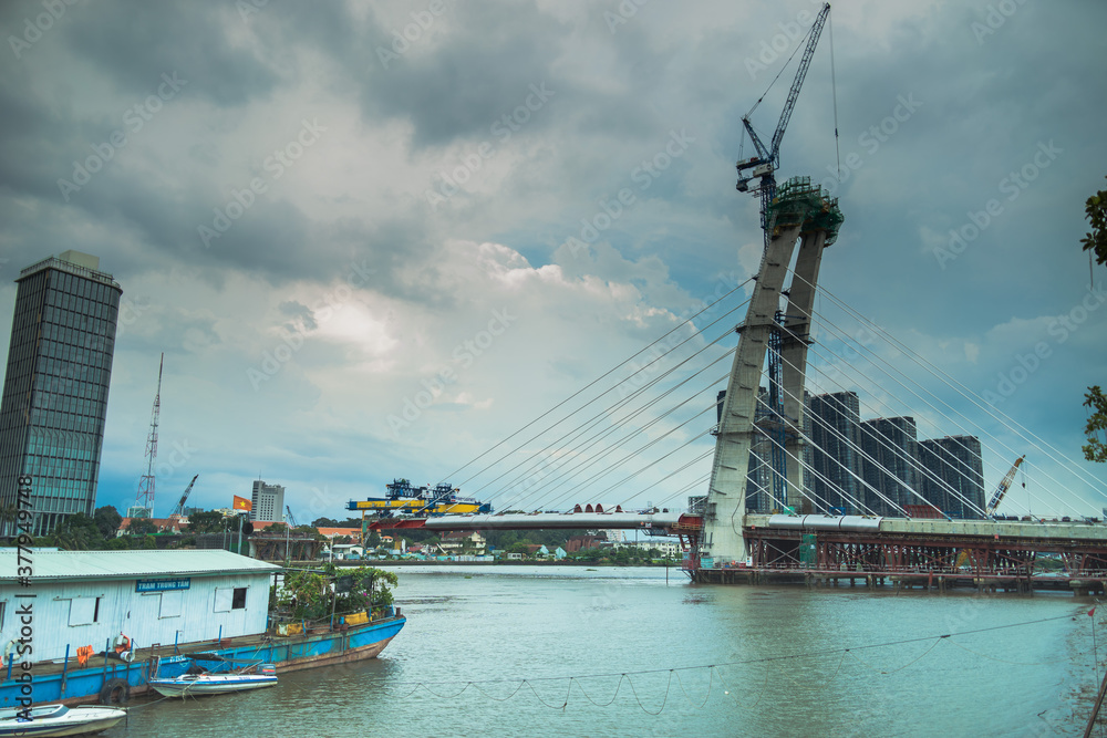 Obraz premium skyline with buildings and Saigon river in sunset, a new cable-stayed bridge is building connecting Thu Thiem peninsula and District 1 across the Saigon River.
