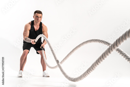 Attractive muscular man working out with heavy ropes. Photo of handsome man in sportswear isolated on white background. Crossfit © zamuruev
