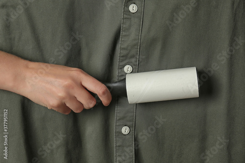 Woman cleaning khaki shirt with lint roller, closeup