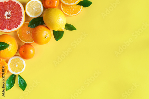 Slices, whole citruses are laid out in composition in upper left corner of background. Tangerines, oranges, grapefruits, lemons, limes are lying on orange yellow canvas. Summer exotic tropical fruits.
