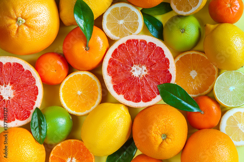 Slices, pieces, whole ripe citruses are on background. Juicy tangerines, oranges, grapefruits, lemons, limes, leaves are on yellow canvas. Summer exotic tropical citrus fruits for preparing juice.