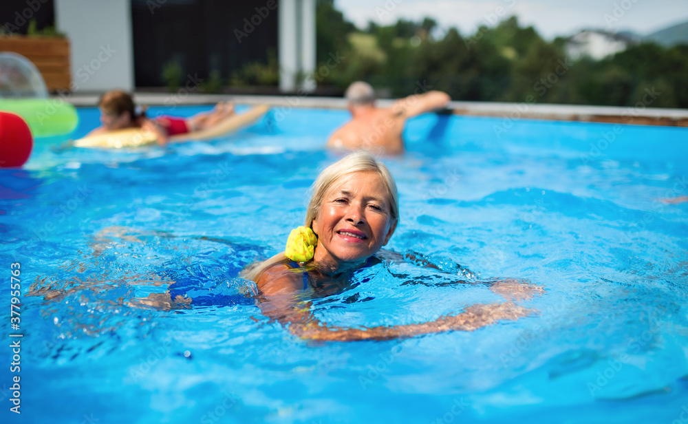 Portrait of senior woman in swimming pool outdoors in backyard, looking at camera.