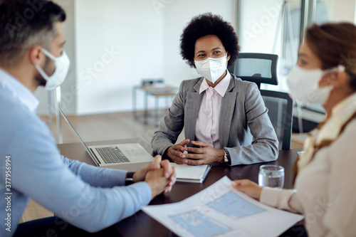 Black real estate agent wearing a face mask while having meeting with her clients in the office. photo