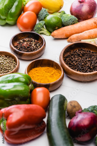 selective focus of fresh ripe vegetables and fruits around bowls with spices on wooden white background