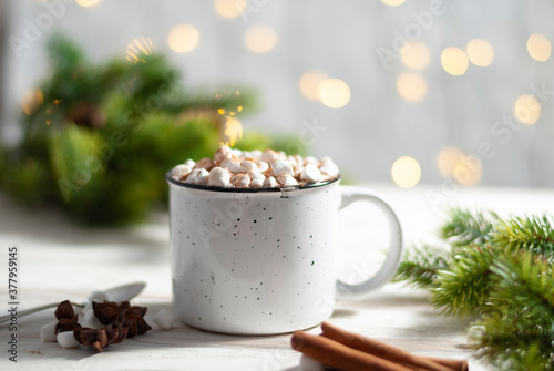 Christmas white cup with hot chocolate and marshmallows on with cinnamon sticks with beautiful garland lights
