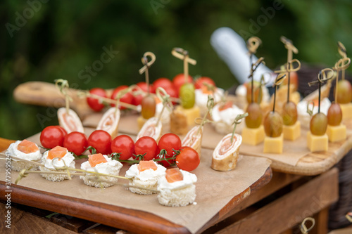 A set of canapes for a snack at a banquet, slices of tomato grapes cheese and fish on wooden boards.