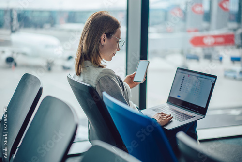 Quadro su tela Young woman traveler using smartphone and laptop at airport