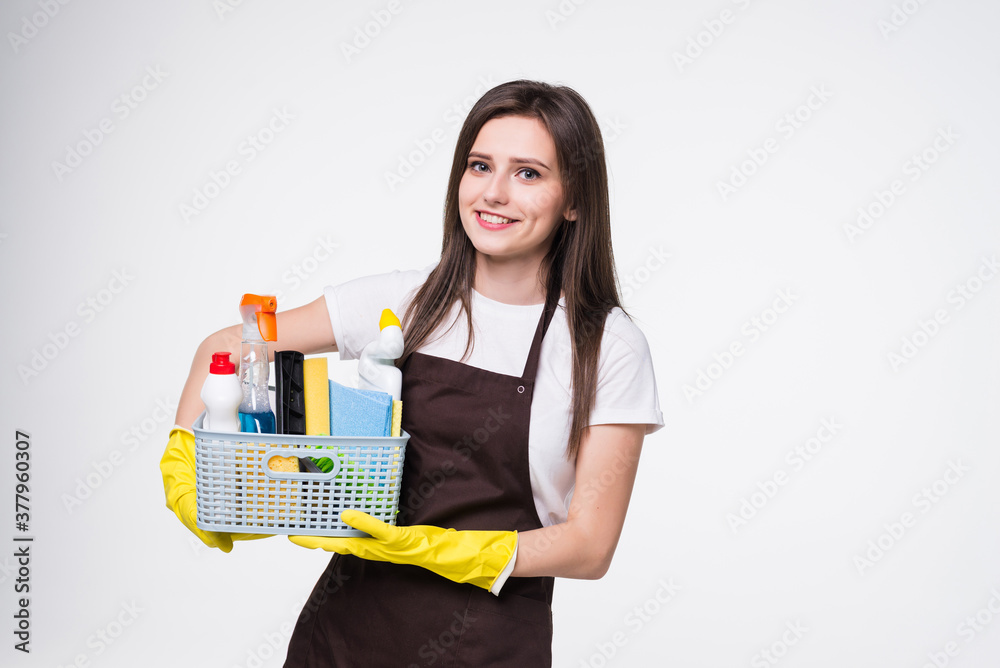 Young attractive smiling housewife wearing casual clothes, latex gloves holding full basin of cleaning agent isolated on white background Young attractive smiling housewife wearing casual clothes, latex gloves holding full basin of cleaning agent isolated on white background