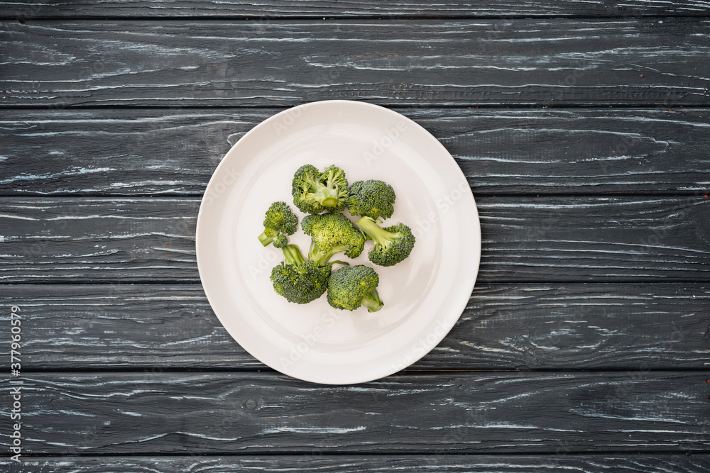 top view of fresh broccoli on plate on wooden surface