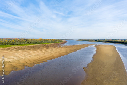 Morning aerial view of a sandbar on the river. In the background is an autumn forest.