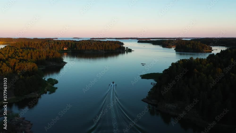 Aerial view following a boat, driving in middle of islands, colorful, summer sunset, in the Swedish Stockholm archipelago, at the Gulf of Bothnia, in Sweden - dolly, drone shot