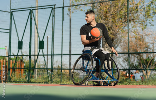 Fotografering Young handsome man in wheelchair at basketball playing ground