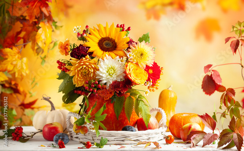 Autumn bouquet of beautiful flowers and berries in a pumpkin on wooden white table. Concept of autumn festive decoration for Thanksgiving day.