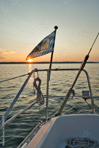 Sailing ship with bavarian flag in the lake or ocean with light waves and sunset