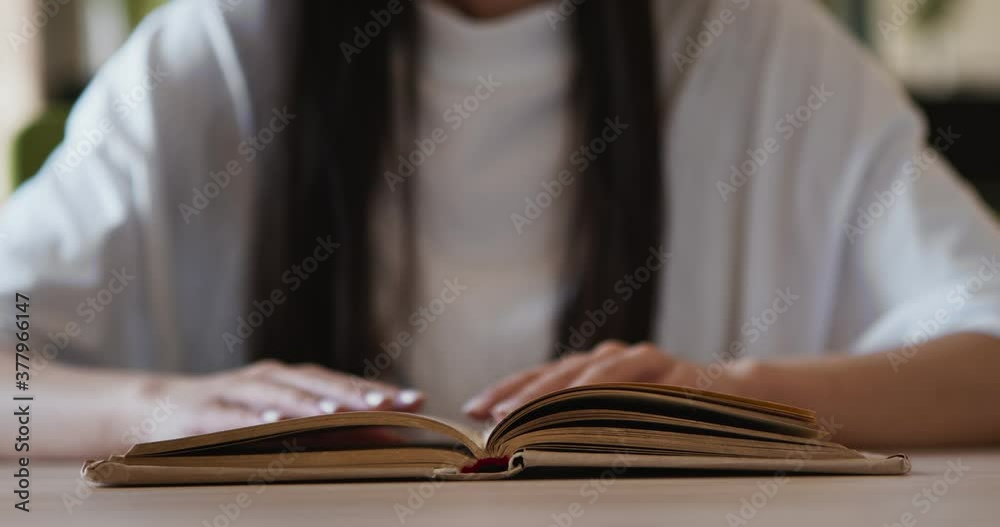 Female student reading old book in library, turning page, close up Female student reading old book in library, turning page, close up