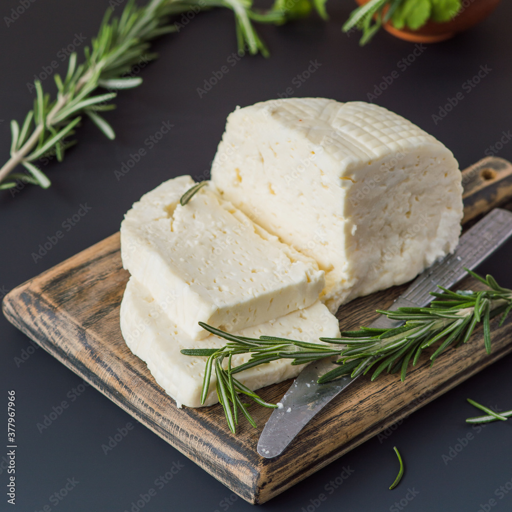 Soft homemade cheese and sprigs of fresh rosemary on a wooden cutting board on a dark background. Selective focus.