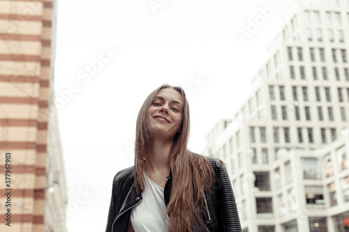 Confident young woman from below looking down at camera. Pretty girl with blonde hair wearing black faux leather jacket. Low angle shot.