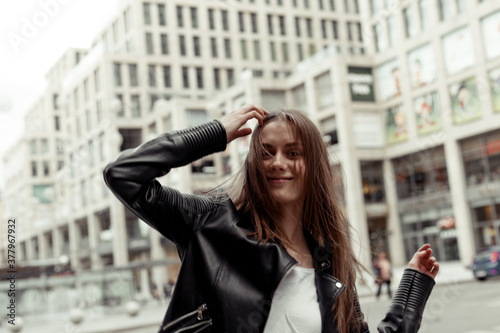 Blonde girl with long windy hair. Portrait of the girl in black faux leather jacket on the building background photo