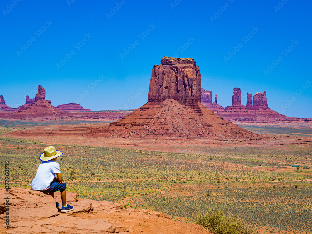 Child with cowboy hat admires panorama from Artist's Point in Oljato Monument Valley, region of Colorado Plateau characterized by cluster of vast sandstone buttes, Arizona Utah border.