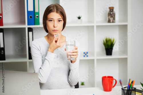 Young woman takes white round pill with glass of water in hand