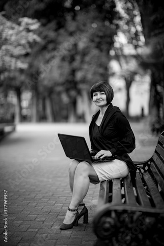 black and white portrait of a woman in business style, with a laptop, on a bench in the Park, working remotely in the field of Economics and accounting.