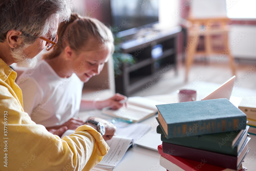 grandfather is interested in his granddaughter's studies at school, help her with homework, they sit with books and notebooks at home grandfather is interested in his granddaughter's studies at school, help her with homework, they sit with books and notebooks at home