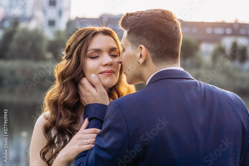 Beautiful caucasian couple kissing by the lake at sunset. Close-up portrait. Honeymoon concept.