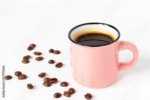 Pink сup of fresh coffee with grains on white wooden background.