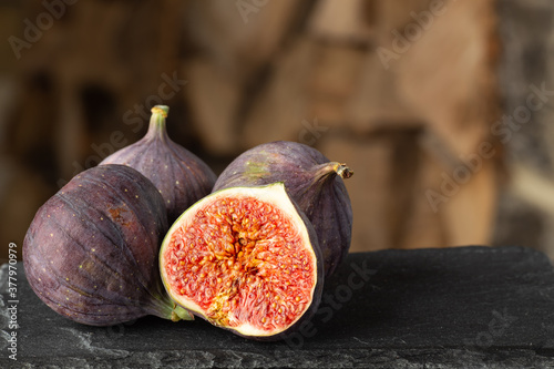Three whole and one cut ripe organic figs on dark rough stone and blurred wooden background