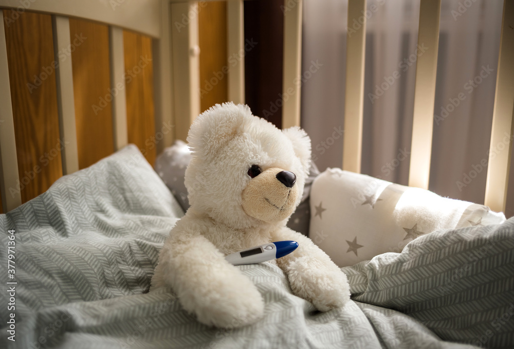 White Teddy bear in a crib with a thermometer White Teddy bear in a crib with a thermometer