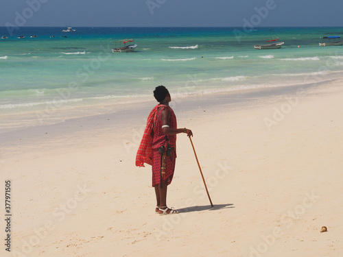 Zanzibar island, Tanzania - 08/07/2020: African man is standing on the white sand beach, near blue Indian ocean