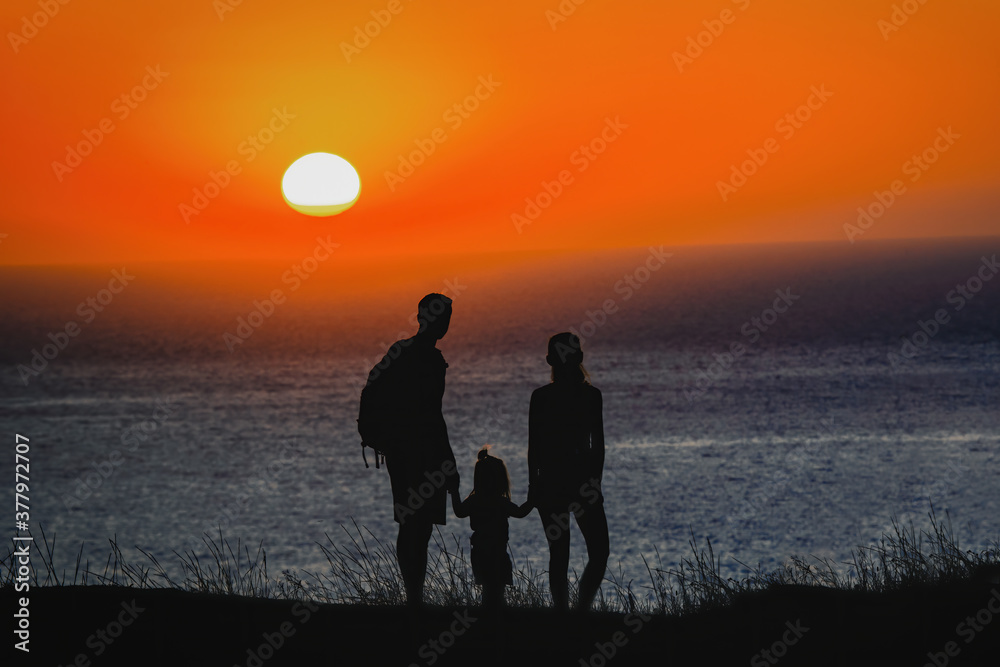 Happy family standing on the background of the sunset sky and sea holding hands. High quality photo