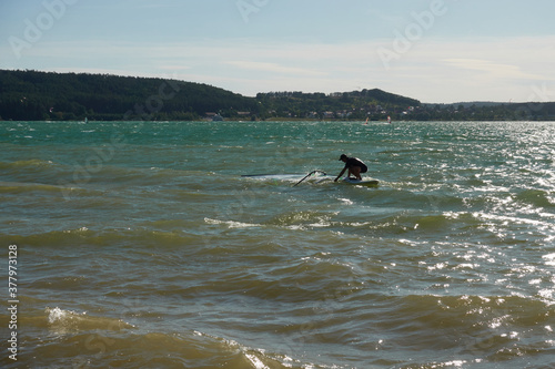 Wind surfer pulls up his sail, blue and brown lake water, hills with trees and blue sky. Copy space. Germany, Brombachsee.