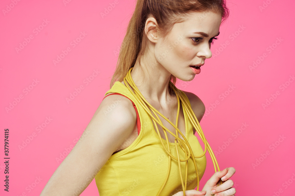 sportive woman jumping rope in hands yellow tank top pink background workout lifestyle