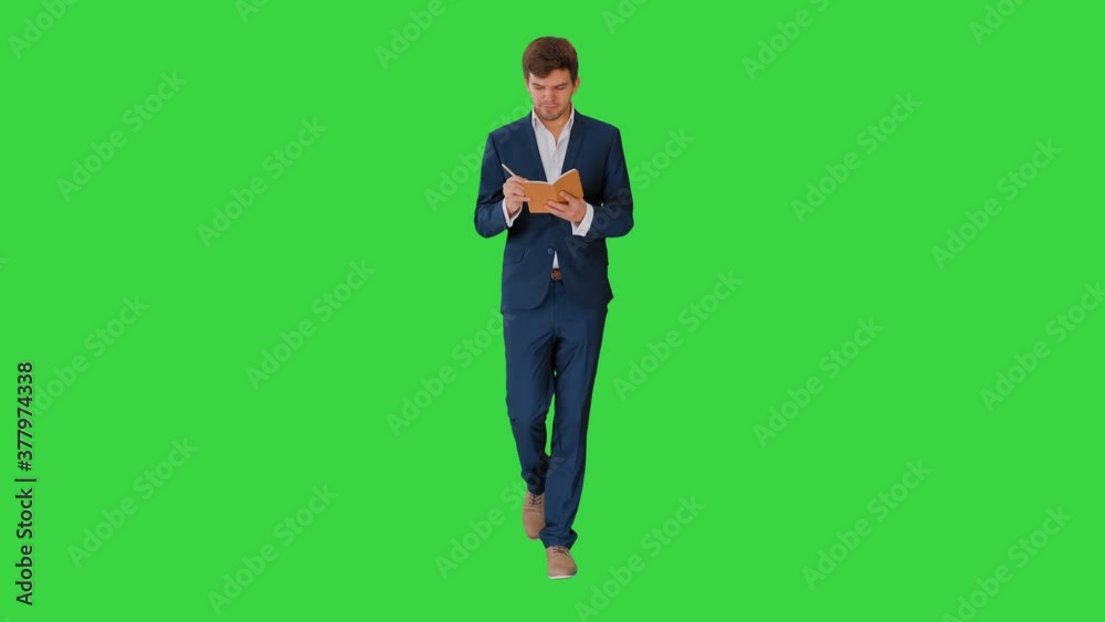 Young businessman thinking and writing notes in his notebook while walking on a Green Screen, Chroma Key. Young businessman thinking and writing notes in his notebook while walking on a Green Screen, Chroma Key.