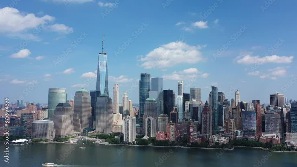 An aerial view of lower Manhattan. The drone dolly out and tilts down. The freedom tower is the main attraction on this day with blue skies and a few clouds. Two boats sail by below on the lower left. An aerial view of lower Manhattan. The drone dolly out and tilts down. The freedom tower is the main attraction on this day with blue skies and a few clouds. Two boats sail by below on the lower left.